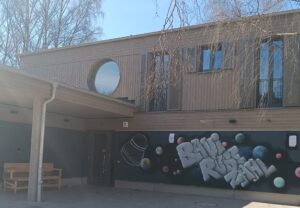 Vorderansicht vom Haus des Bauspielplatz Rübezahl mit dem Schriftzug BAUI RÜBEZAHL und der Eingangstür.