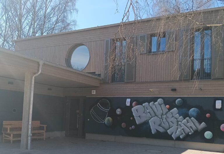 Vorderansicht vom Haus des Bauspielplatz Rübezahl mit dem Schriftzug BAUI RÜBEZAHL und der Eingangstür.