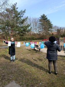 Zwei Frauen schmücken draußen eine bunte Wimpelkette mit Ballons und A4-Plakaten.