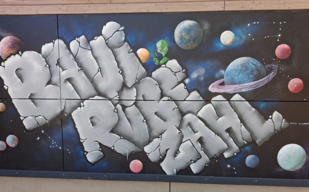 Schriftzug BAUI RÜEBE ZAHL auf dunkler Wand und Planeten