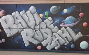 Schriftzug BAUI RÜEBE ZAHL auf dunkler Wand und Planeten