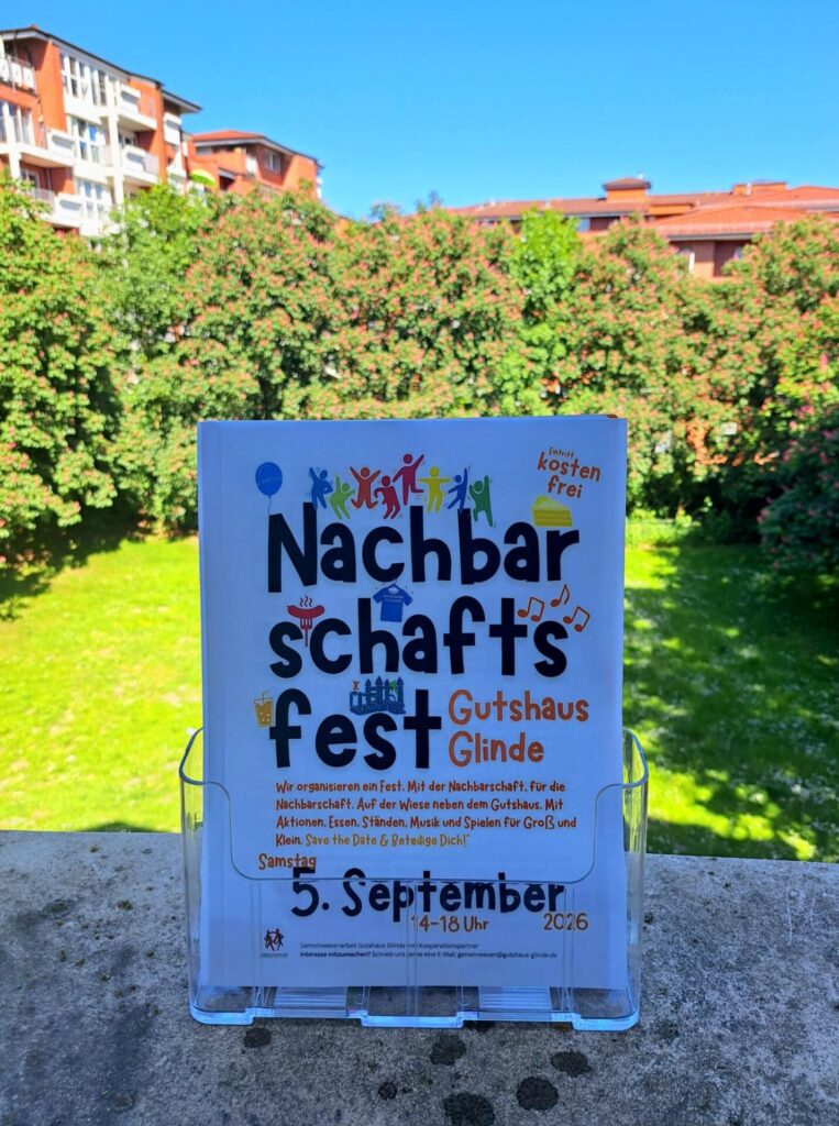Foto von einem Flyer des Nachbarschaftsfest auf dem Balkon im Gutshaus Glinde. Im Hintergrund die Wiese auf der das Nachbarschaftsfest stattfinden wird