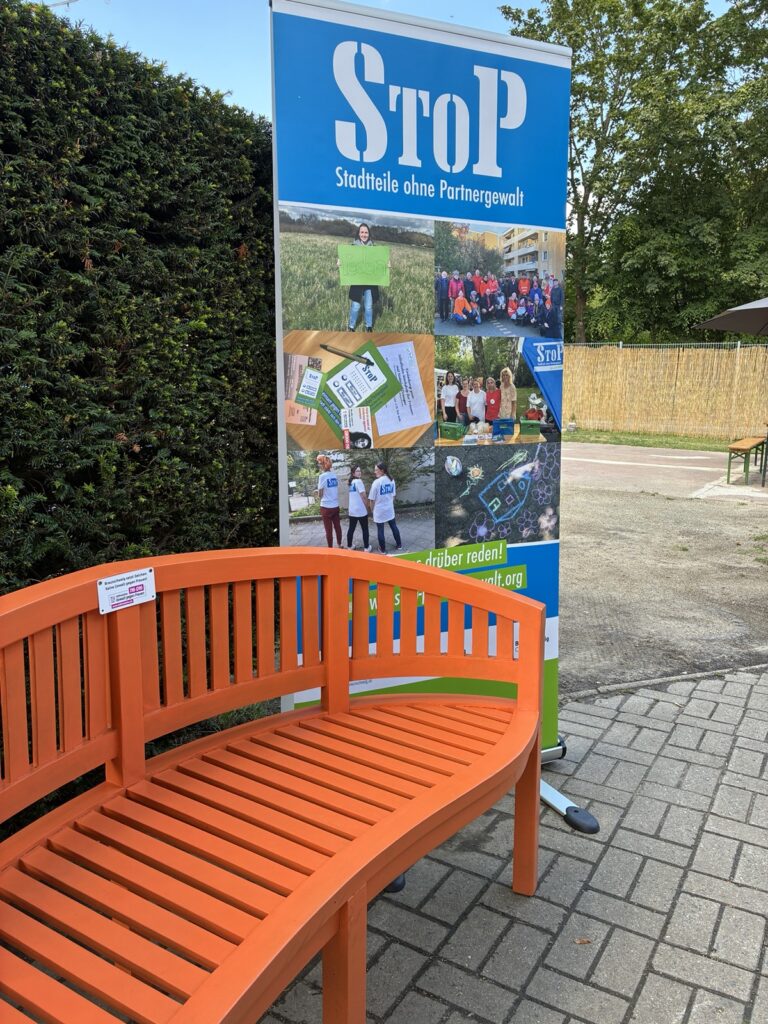 Orangefarbene Bank mit Hilfetelefon und StoP Roll-Up